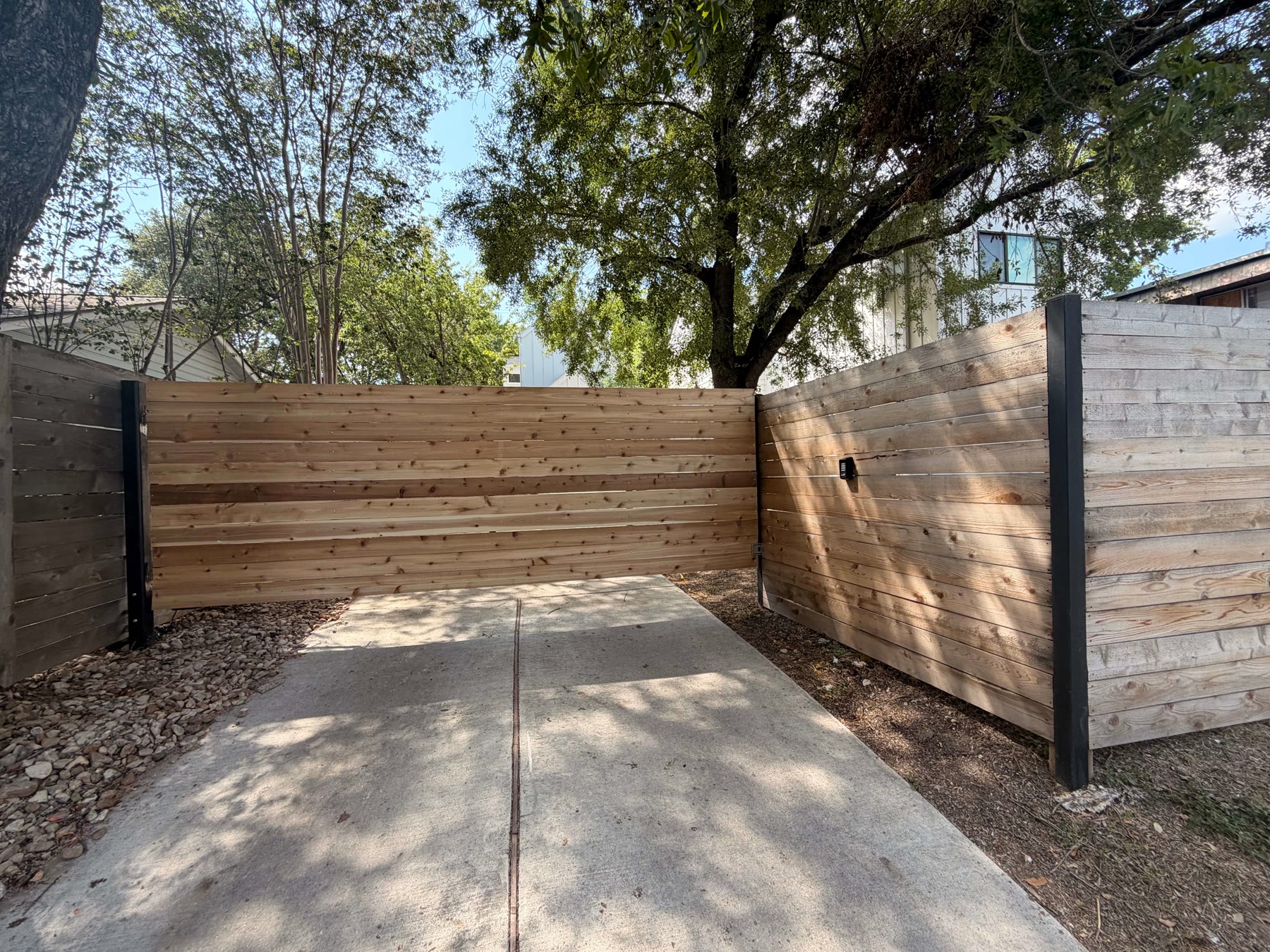 Sid’s cedar swing gate closed across the driveway between black steel posts, with the keypad mounted on the fence