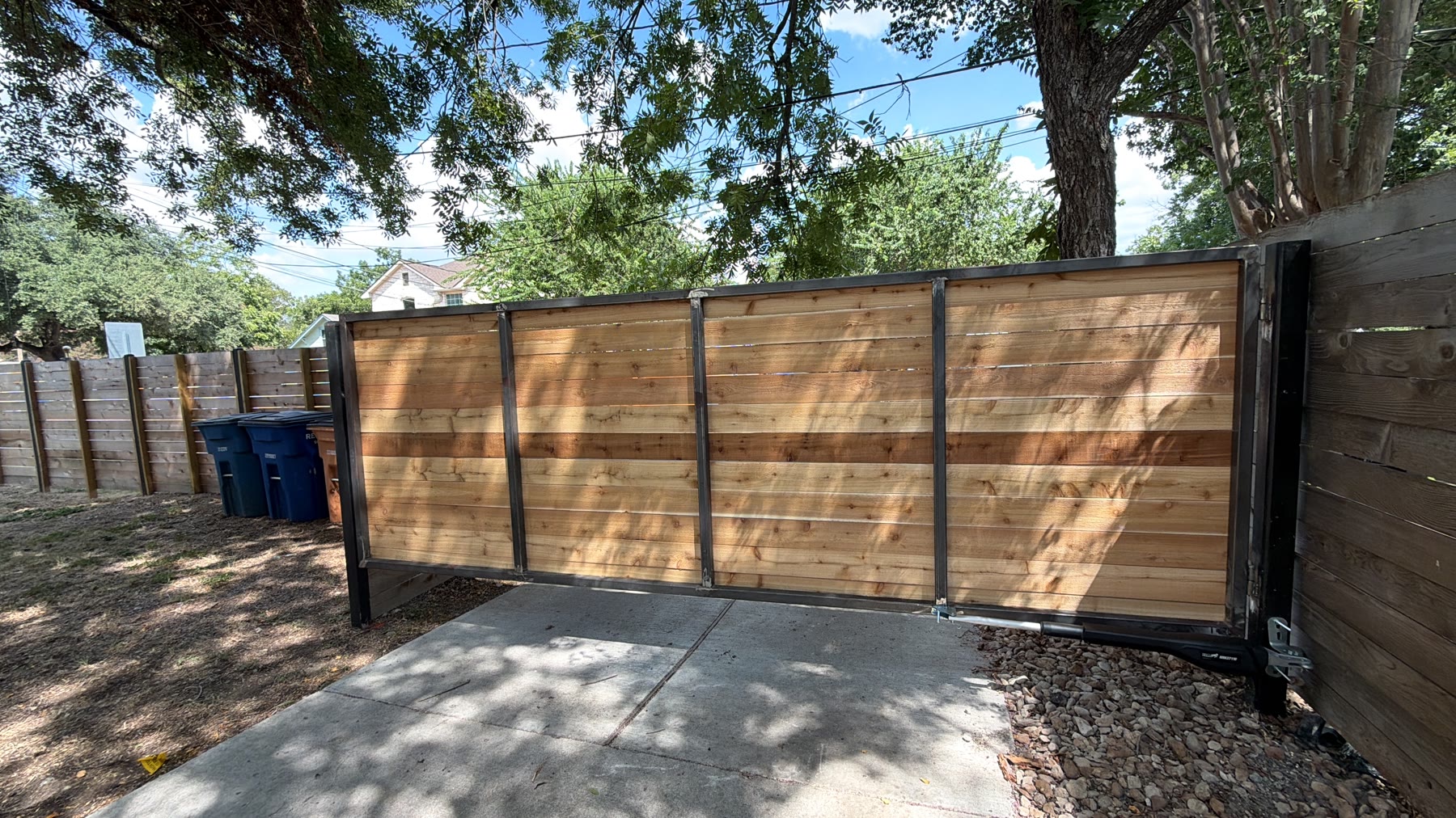 Welded black steel frame and cedar panels of Sid’s gate with the automatic swing-arm opener at the hinge post